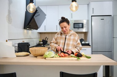 Bir kadın kendi mutfağında taze sebzeleri dilimler, canlı ve sağlıklı bir salata yaratır. Modern mutfak düzeninde sıcaklık, sağlık ve aşçılık yaratıcılığı duygusu yayılıyor..