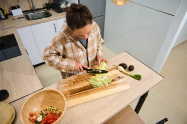 İyi aydınlatılmış modern bir mutfakta sebze doğrayan bir insan. Sahnede taze ürünler, sıcak bir atmosfer ve sağlıklı yaşam ve ev yapımı yemekler sergileniyor..