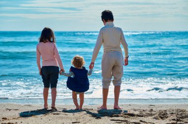 Üç çocuk okyanusun kenarında çıplak ayakla güneşli yaz anlarının sıcaklığının ve birlikteliğinin tadını çıkarıyorlar..