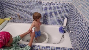 Süslü mavi mozaik döşemeleri olan bir banyoda bir bakıcı tarafından yıkanan bir bebek..