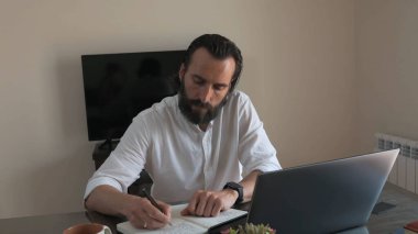 Profesyonel adam notlar alırken konsantre oluyor ve rahat bir yerde dizüstü bilgisayarla çalışıyor..