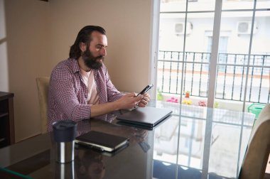 Modern bir çalışma alanında cam bir masada akıllı telefon kullanan genç bir adam işe odaklanıyor..