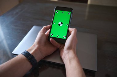 Yakın plan çekimde, ahşap bir masada dizüstü bilgisayarı yeşil ekranlı bir akıllı telefonu tutarken içeriği hazırlıyorum..