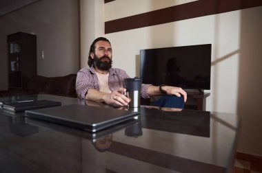 Genç bir profesyonel, iş aletlerinin yanında oturarak ev ofisinde rahatlıyor. Bir anlık yansıma..