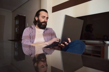 Samimi bir ofis ortamında dizüstü bilgisayarla çalışan düşünceli bir genç. Atmosfer odaklanma ve gevşemeyi vurguluyor, serbest projeler, çevrimiçi işler ve üretkenlik için mükemmel.