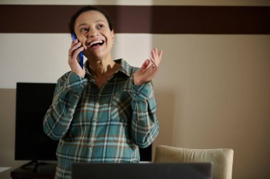 Ekose giyen neşeli bir kadın ev ofis ortamında akıllı telefonuyla konuşur. Sahne, dengeli bir modern yaşam tarzını sembolize ederek bağlantı, sıcaklık ve üretkenliği aktarıyor..