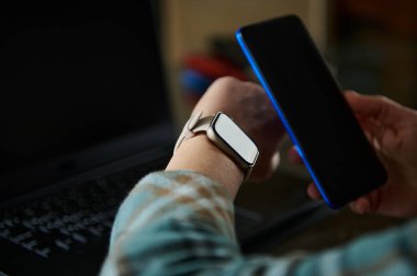 Bir kişi ofis ortamında akıllı telefon ve akıllı telefon ile iletişim kurarak günlük hayatta teknolojiyi vurguluyor. Sahne modernlik, verimlilik ve teknolojik bütünleşme kavramlarını somutlaştırıyor.