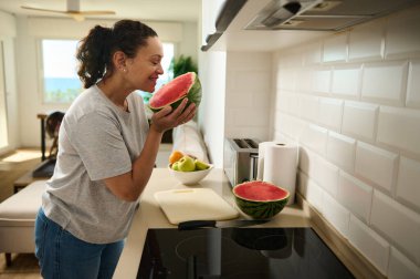 Günlük mutfak ortamında bir kadın taze kesilmiş karpuz kokusunun tadını çıkararak sıcak ve sağlıklı bir ev hayatını sembolize eder..