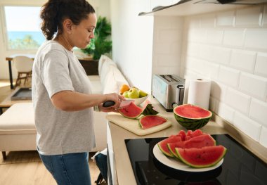 Bir kadın mutfak tezgahında taze karpuz dilimliyor, açık ve sağlıklı bir yemek hazırlama sahnesi sergiliyor, rahatlama ve rahatlama yayıyor..