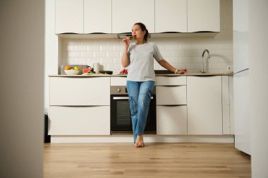 Temiz, modern bir mutfakta, tezgahın yanında atıştırmalıklardan hoşlanan bir kadının olduğu sıradan bir an..