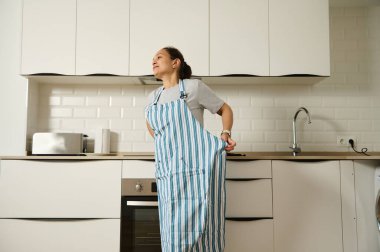 Genç bir kadın, temiz ve modern bir mutfakta yemek pişirmeye ev hayatını ve sağlıklı yaşamı teşvik etmeye hazırlanıyor. Tasarım, parlak bir ortamda aile ve sade bir atmosferi vurguluyor..