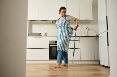 Bir kadın çizgili önlüğünü şık bir mutfakta bağlıyor. Parlak mutfak modern tasarımı içerir ve düzenli bir şekilde düzenlenir, dinginlik duygusu ve ev hayatına odaklanır..