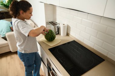 Bir kadın mutfak tezgahında karpuz hazırlıyor, sağlık ve ev hayatı temalarını çağrıştırıyor..