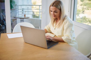 Modern bir ofiste odaklanmış bir kadın dizüstü bilgisayarı üzerinde çalışıyor ve bir proje planlıyor. Sahne üretkenlik ve pozitif bir çalışma ortamı sergiliyor, bağlantı ve motivasyonu vurguluyor.