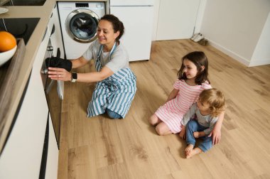 Neşeli çocukları onu gözlemlerken bir anne havadar, modern bir mutfakta yemek pişirir. Sahne, sıcaklıkla, yaratıcılıkla ve birliktelikle dolu bir aile sabahı yakalıyor..