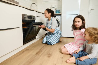 Bir anne, çocuklarının dikkatle izlediği modern bir mutfakta taze kruvasan pişirir. Konforlu ve çekici an, iyi aydınlatılmış bir evde aile bağlarını ve sağlıklı yemek hazırlıklarını gözler önüne seriyor..