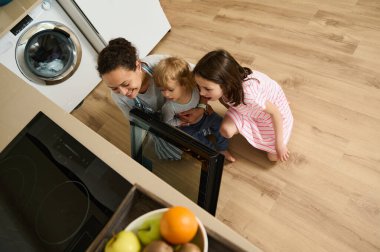 Üç kişilik bir aile, birlikte yemek pişirirken mutlu bir şekilde mutfakta etkileşime geçiyorlar. Anne ve çocuklar, sevgi dolu ve sıcak bir çevreye katkıda bulunarak, neşe ve beraberlik anlarını paylaşıyorlar..