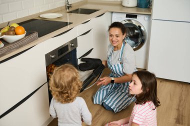 Bir anne, çocukları izlerken modern bir mutfakta ev yapımı kruvasan hazırlar. Sahne sıcaklığı, aile birlikteliğini ve ışık dolu bir evde birlikte vakit geçirmenin neşesini yansıtıyor..