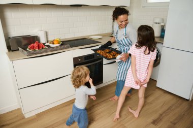Anne taze hamur işleri sunarken, çocuklar sıcak, güneşli bir mutfakta kahkahalar atarken neşeli bir aile anı..