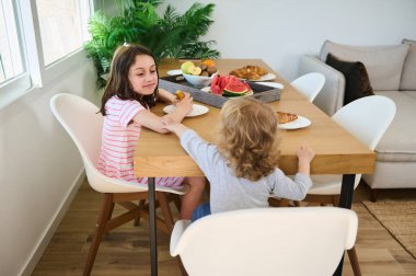 Bir aile evde birlikte sağlıklı bir kahvaltı yapar. Çocuklar, sıcaklığı ve birlikteliği yansıtan parlak, modern bir yemek salonunda taze kruvasanlarla ve meyvelerle anlar paylaşırlar..