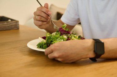 Akıllı gözlüklü bir adam kapalı bir masada taze, renkli bir salatanın tadını çıkarıyor. Sahne sağlık odaklı bir yaşam tarzı sunuyor, besleyici yiyecekleri gündelik bir ortamda vurguluyor.