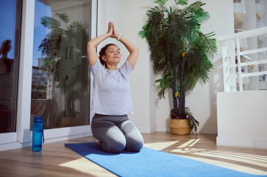 Güneşli bir odada, yeşil ve taze dekorlu bir odada yoga yapan bir kadın farkındalık, rahatlama ve sağlık gelişimi üzerine yoğunlaşıyor..