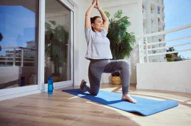 Bir insan terasta yoga pozu veriyor, sağlıklı yaşam ve iç dengeyi gösteriyor. Huzurlu kentsel arka plan rahatlatıcı bir dokunuş ekler.