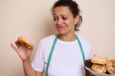 Sağlıklı alternatifler düşünürken elinde bir tabak donut tutan bir kadın dengeli beslenme ve sağlıkla ilgili seçenekleri sembolize ediyor..