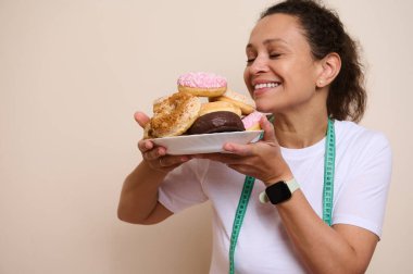 Gündelik giyinen neşeli bir kadın, elinde çeşitli bir tabak donut tutarken gülümser, sağlık ayı kutlamaları sırasında hoşgörü ve beslenme dengesini sembolize eder..