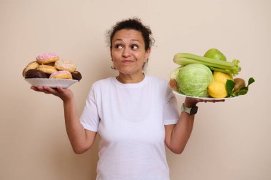 Bir elinde çeşitli donutlar, diğer elinde bir tabak taze sebze ve meyve tutan kişi sağlık aylarında hoşgörü ile sağlık arasında karar veriyor..