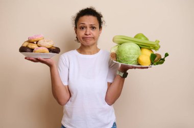 İki tabak tutan bir kadın, biri renkli çöreklerle, diğeri taze meyvelerle, sağlıklı yaşam tarzını ve hoşgörüyü temsil ediyor. Diyet, sağlık ve sağlıkla ilgili konular için mükemmel..