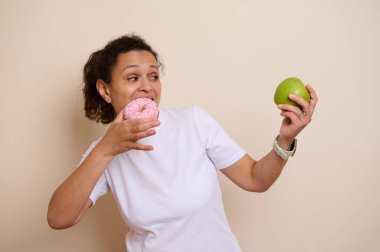 Beyaz gömlekli bir kadın, pembe serpilmiş bir çörekle yeşil bir elma arasındaki ikilemi düşünür. Sağlıklı beslenme ve hoşgörü arasındaki tercihleri sembolize eder..