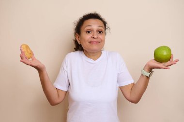 Şekerli çörekle taze yeşil elma arasında tartışan bir kadın. Görüntü, hoşgörü ile günlük seçimlerdeki sağlıklı alternatifleri dengeleme kavramını betimliyor..