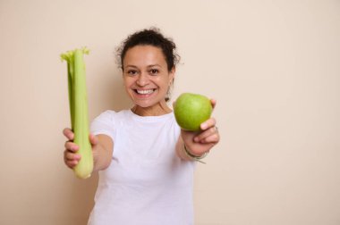 Enerjik bir kadın canlı bir yaşam tarzı için dengeli ve sağlıklı bir diyetin önemini vurgulayan taze, sağlıklı kereviz sapları ve yeşil bir elma sunar..