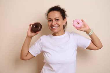 Beyaz tişörtlü neşeli bir kadın iki çeşit donut tutmaktan hoşlanır, biri çikolatayla kaplıdır, diğeri ise pembe şekerle kaplıdır, neşe ve hoşgörü taşır..