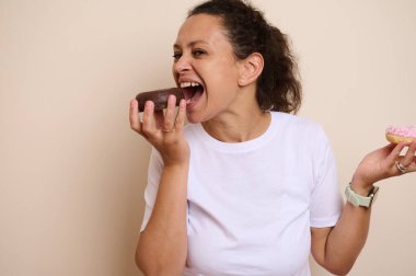 Gülümseyen bir kadın elinde iki lezzetli çörek tutuyor, keyifli bir şekilde bu leziz ikramların tadını çıkarıyor. Görüntü, tatlı tatlılardan zevk almanın neşesini ve şımarıklığını yakalar..