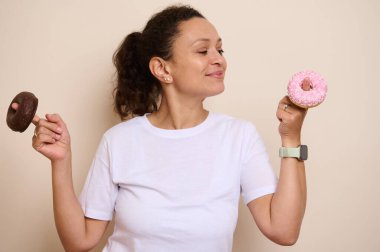 Neşeli bir kadın donutla poz veriyor, biri çilekli buzlu, diğeri de çikolata kaplı, şekerli zevklerin vücut bulmuş anları. Onun ifadesi keyfi bir ortamda memnuniyet ve neşe taşıyor..