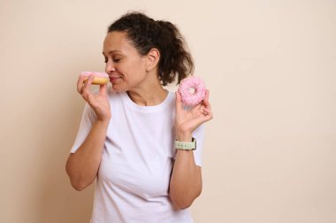 Neşeli bir kadın, kokularının tadını çıkaran iki pembe donuta değer veriyor. Hoşgörü ve mutluluğu temsil eden bu sahne mutluluk ve yemek zevkini çağrıştırıyor..