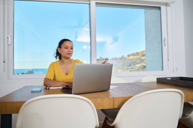 Kendini işine adamış bir profesyonel, sakin bir ofisteki ahşap bir masada dizüstü bilgisayar kullanarak rahat ve resimli bir ortamda odaklanmış bir ilişkiyi yansıtıyor..