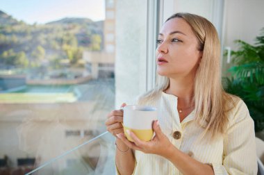 Bir kadının bir kupayı tuttuğu ve dışarıdaki gün ışığıyla pencerenin kenarına yansıttığı huzurlu ve düşünceli bir ortam yarattığı bir an..