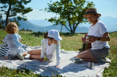 Bir aile güneşli bir dağ gününde piknik yaparak, doğanın tadını çıkararak ve bu huzurlu doğa ortamında birlikte vakit geçirir..