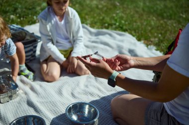 Bir aile bahçede piknik yaparak, güneşli bir günde doğanın tadını çıkararak ve bağ kurarak kaliteli zaman geçirir. Çocuklar bu rahatlatıcı ortamda eğleniyorlar..