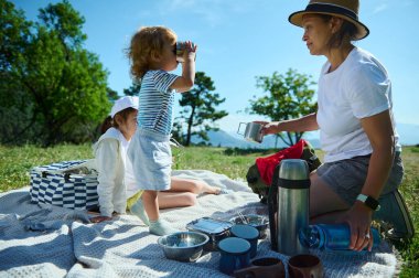Huzurlu bir dağ ortamında neşeli bir aile pikniği. Açık hava yemek gereksinimleriyle doğal ortamda bağ kurma ve keyif alma anları..