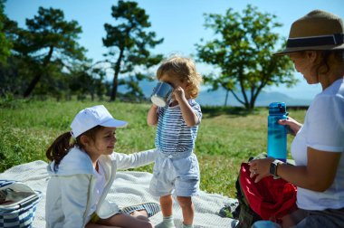 Açık havada yaz pikniğinin tadını çıkaran sevgi dolu bir aile. Ulusal Piknik Ayı ve Ulusal Dışarıda Yemek Günü 'nde yakınlığı, doğayı ve birlikteliği temsil eden ideal betimleme..