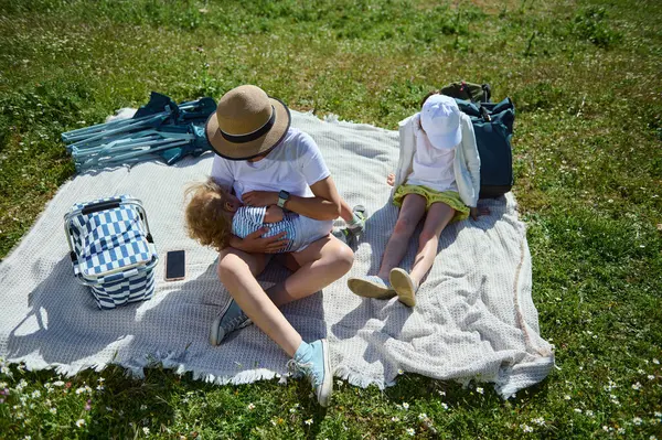 Bir aile açık havada güneşli bir piknik sırasında kaliteli zaman geçirir. Ulusal Piknik Ayı ve Dağ Günü kutlamalarının sıcaklığını somutlaştırarak, doğa ile çevrili gevşeme ve bağlanma anlarından hoşlanırlar..