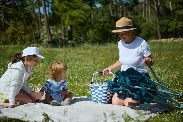 Çocuklarla dolu bir aile güneşli bir günde, yemyeşil ağaçlarla çevrili bir arazide piknik yapıyor, doğal ortamının tadını çıkarıyor..