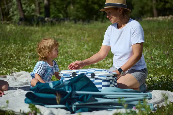 Bir anne ve çocuk olarak yemyeşil, doğal bir çayırda keyifli bir piknik sırasında ortaya çıkan neşeli bir an. Aile, doğa ve açık hava rahatlığının özünü yakalar..