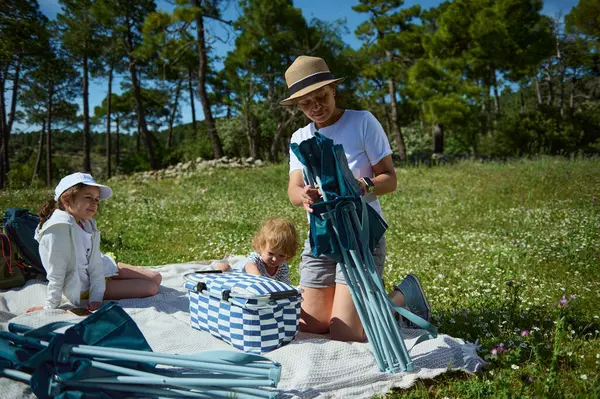 Sevgi dolu bir aile birlikte dışarıda vakit geçirir, kamp malzemeleri toplar ve dağlarda güneşli bir günde doğanın tadını çıkarırlar. Ulusal Piknik Ayı ve Aile Bağları.