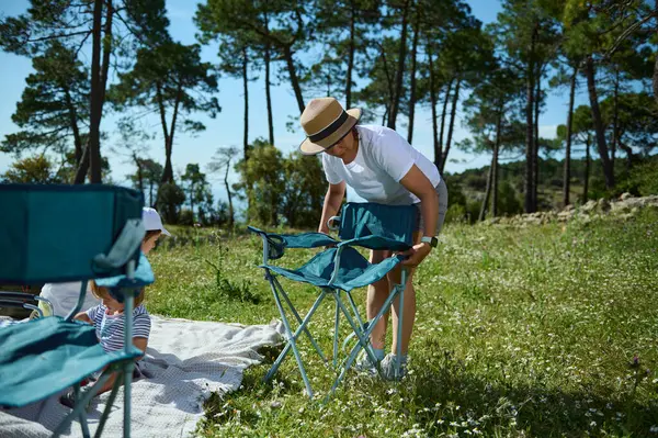 Güneşli bir günde bir aile pikniğe hazırlanıyor. Ağaçların ve çiçek açan çayırların olduğu doğal bir bölgede. Açık havada kaynaşmanın ve eğlencenin sembolü..