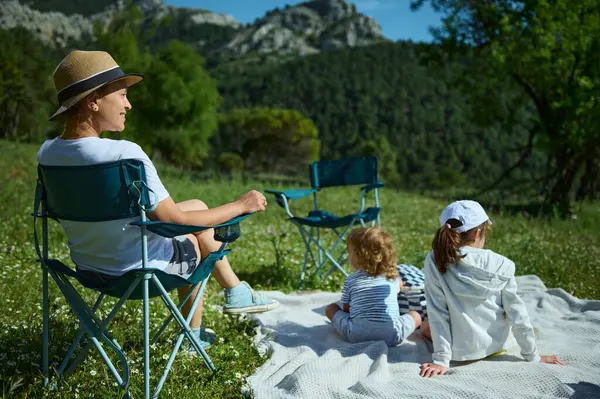 Bir aile dağ pikniği sırasında rahatlar, güneşin altında manzaranın ve doğanın tadını çıkarırlar. Bu görüntü, güzel bir ortamda aile bağlarının ve boş zamanların bir anını yakalar..